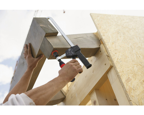 Muž upevňuje drevenú konštrukciu skrutkovou svorkou