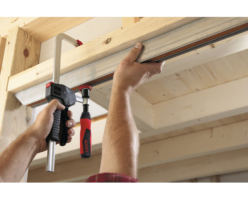 Muž pripevňuje kovový profil ku drevenej konštrukcii pomocou skrutkovej svorky