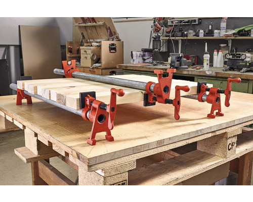 Drevené dosky sú upevnené rúrkovými svorkami na pracovnom stole.