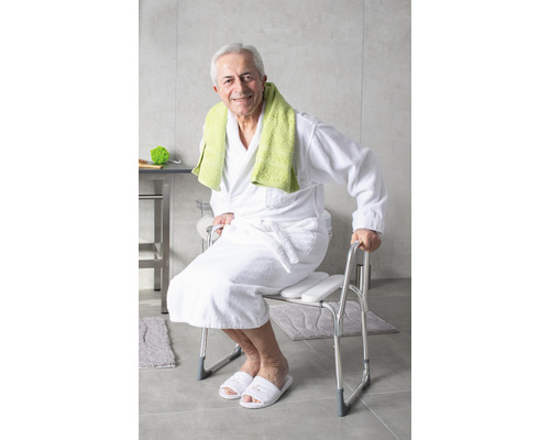 Muž sedí na sprchovacej stoličke s opierkami na ruky v kúpeľni.