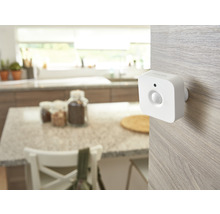 Biely pohybový senzor Philips Hue namontovaný na svetlom drevenom povrchu vo svetlej, organizovanej kuchyni.