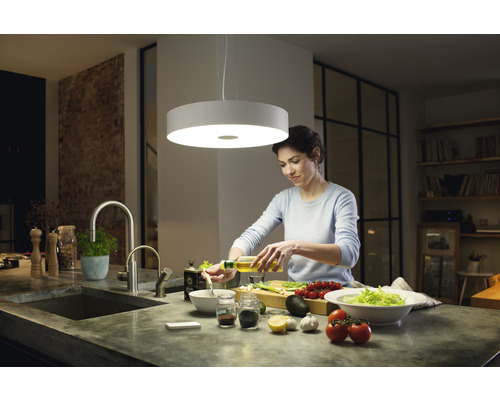 Žena pripravuje šalát pod okrúhlym stropným svietidlom v kuchyni