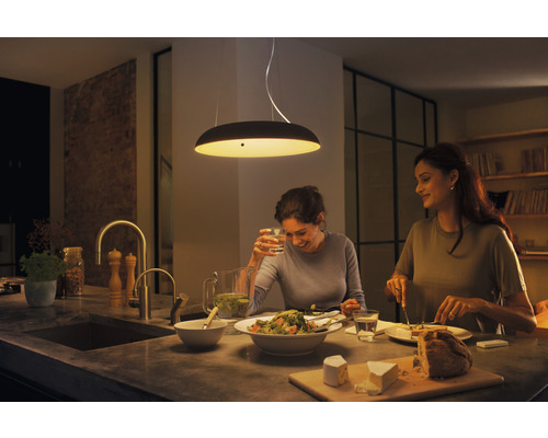 Dve ženy sedia pri kuchynskom stole pod závesným svietidlom a jedia.