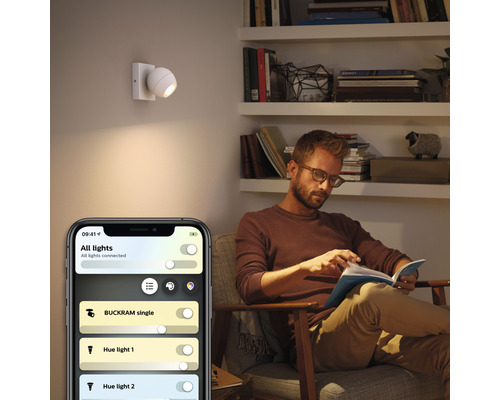Scéna obývačky s mužom čítajúcim knihu a nástenným svietidlom ovládaným aplikáciou