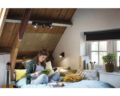 Útulná podkrovná izba s dreveným stropom a stropným svietidlom, kde mladá žena číta v posteli