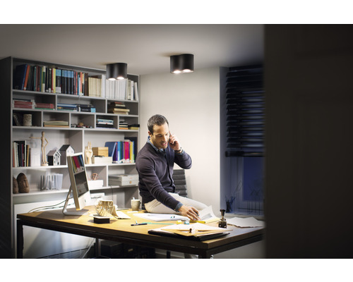 Muž sedí na stole v pracovni so stropnými svietidlami a policami