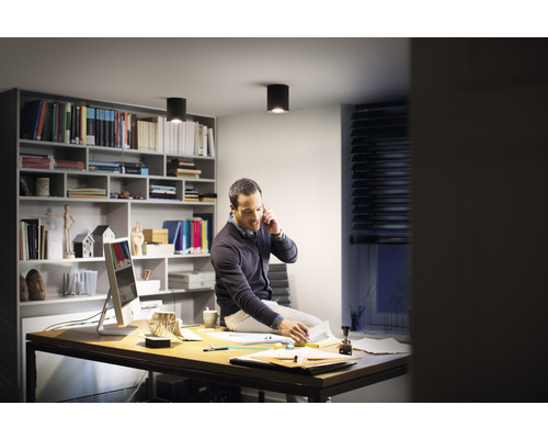 Muž telefonuje na stole pod stropnými svietidlami v pracovni.