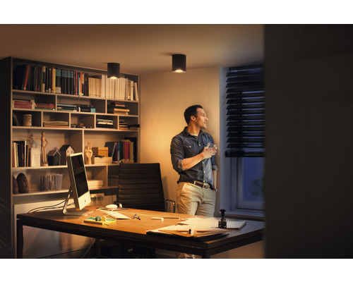 Moderná kancelária s písacím stolom, knižnicou a stropnými svietidlami pre svetlé a organizované pracovné prostredie.