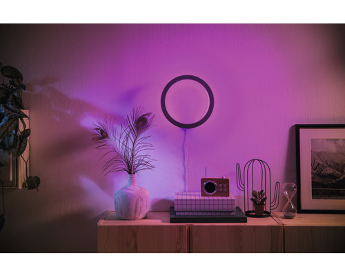 Obývacia izba s kruhovým nástenným svietidlom, váza s pávími perami a dekoratívnymi prvkami na skrinke.