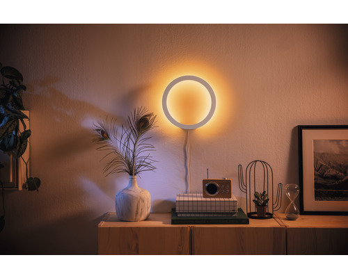 Dekoratívne kruhové nástenné svietidlo nad príborníkom s dekoráciami.