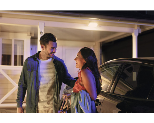 Muž a žena sa smejú pred domom s vonkajším osvetlením a autom.