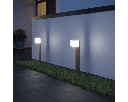 Dve záhradné svietidlá osvetľujú cestu a trávnik pred stenou.