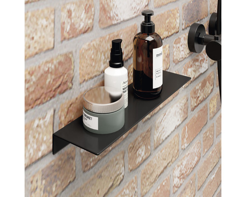 Čierna nástenná polica v kúpeľni s ošetrujúcimi produktmi na pozadí z tehál.