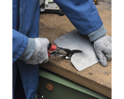 Osoba strihá kus kovu nožnicami na plech.