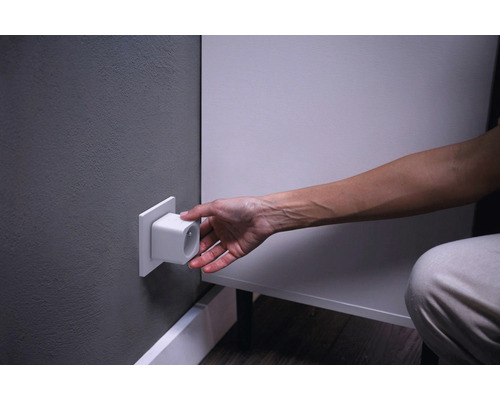 Osoba zapája biely adaptér do zásuvky v stene.