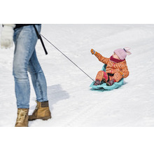 Dieťa sedí na saniach a ťahá ho osoba.