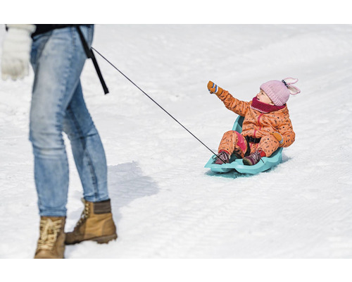 Dieťa sedí na saniach a ťahá ho osoba.