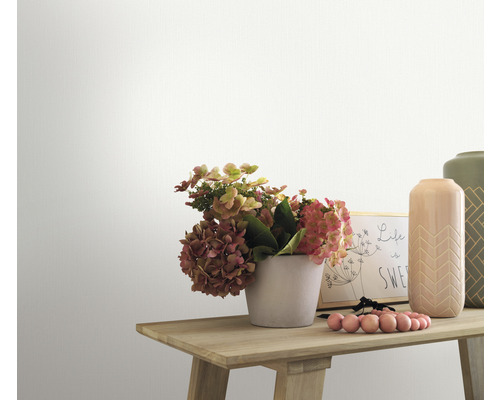 Detail zdobeného dreveného stola s kvetmi, vázami a rámom na fotografie pred bielou stenou