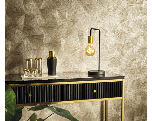 Ukážka vybavenia s komodou, lampou, pohármi a vzorovanou tapetou.