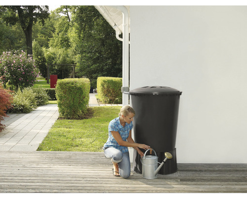 Žena plní kanvicu pri sude na dažďovú vodu v záhrade