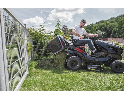 Muž vysýpa kôš na trávu záhradného traktora na trávnik