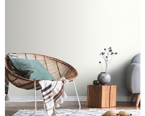 Dekoratívna obývacia izba s ratanovým kreslom, dreveným stolom a svetlými stenami