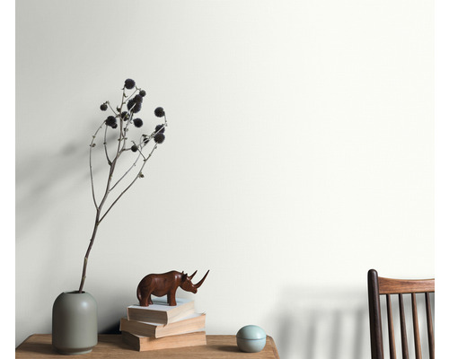 Obývacia izba s aranžmánom vázy, dekoratívneho objektu a stohu kníh pred natretou stenou.