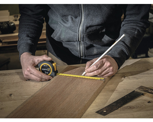 Osoba meria drevenú dosku 5-metrovým zvinovacím metrom Stabila a označuje ju ceruzkou.