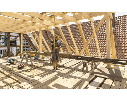 Tesár pri konštrukcii strechy s drevenými krokvami a meracím nástrojom.