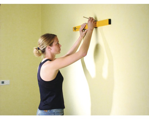 Žena označuje miesto na stene ceruzkou a vodováhou