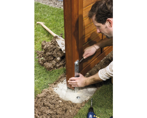 Muž montuje stĺpik plota s kľúčom na betónový základ v záhrade.