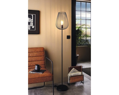 Kovová stojaca lampa s drôteným tienidlom v obývacej izbe.