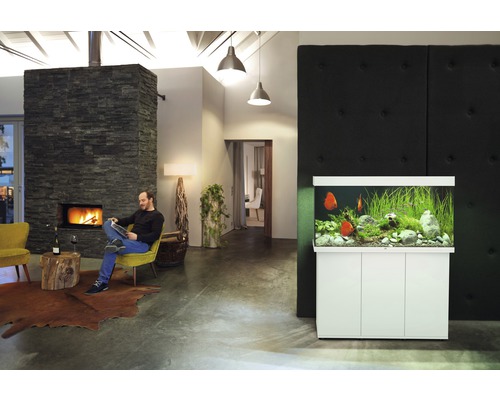 Obývacia izba s akváriom a mužom sediacim pri krbe.