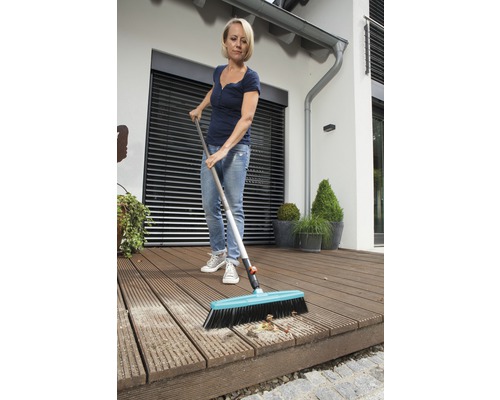 Žena zametá drevenú terasu metlou.