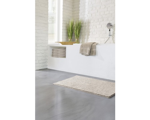 Svetlá kúpeľňa s kúpeľňovou predložkou, uterákmi a dekoráciou na murovanej vani.