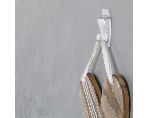 Dekoratívne drevené srdce visí na priehľadnom lepiacom háčiku na stene.