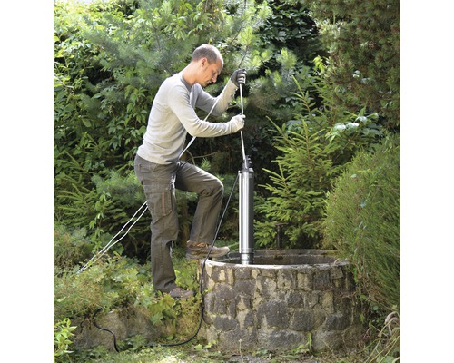 Muž inštaluje hlbinné čerpadlo do studne v záhrade.