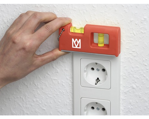 Ruka drží vodováhu na elektrickej zásuvke, aby skontrolovala vyrovnanie.