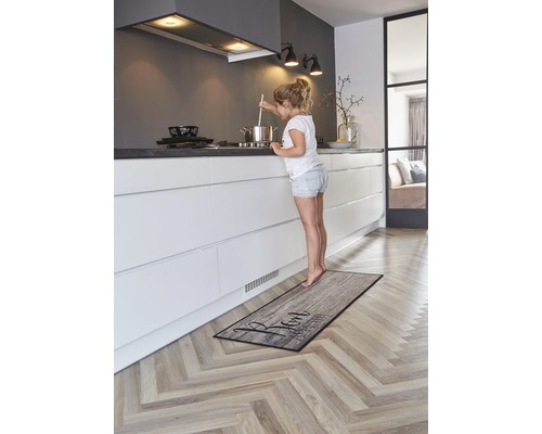 Kuchyňa s kuchynským kobercom v drevenom dizajne a mladé dievča pri sporáku