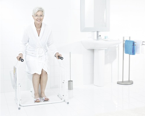 Svetlá kúpeľňa s toaletou, umývadlom a staršou ženou používajúcou toaletnú pomôcku