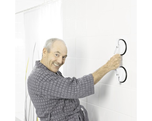 Muž v župane pripevňuje držadlo s prísavkami na obkladanú stenu.