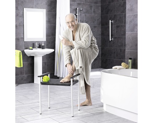 Kúpeľňa s vaňou, umývadlom a osobou sediacou na sprchovej stoličke