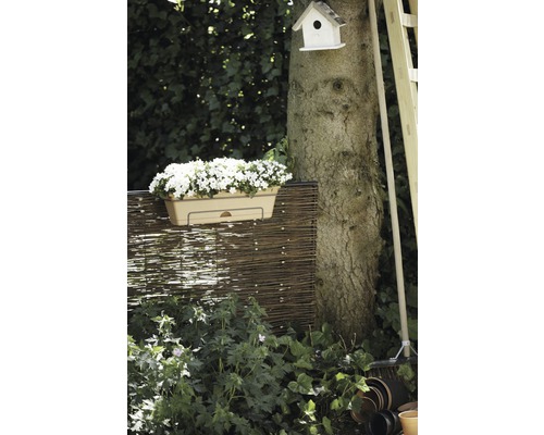 Záhradná scéna s kvetináčom, prúteným plotom, kmeňom stromu, vtáčou búdkou a záhradným náradím.