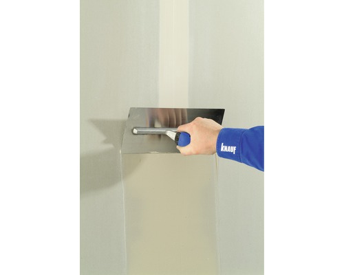 Osoba vyhladzuje stenu pomocou hladidla a tmelu.