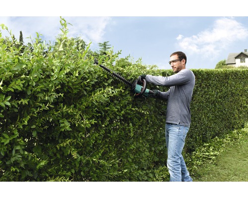 Muž strihá živý plot pomocou nožníc na živý plot