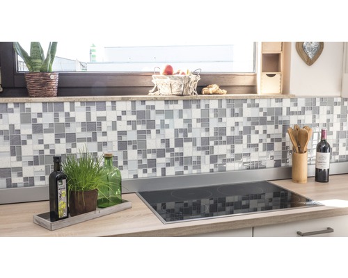 Kuchynská scéna s mozaikovými obkladmi na stene a varnou doskou na pracovnej doske.