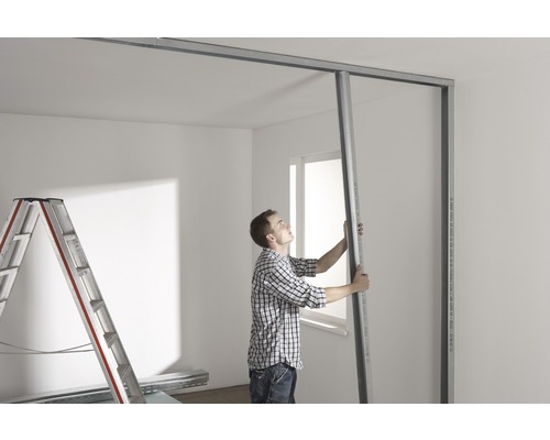 Muž montuje kovové profily pre sadrokartónovú stenu v miestnosti.