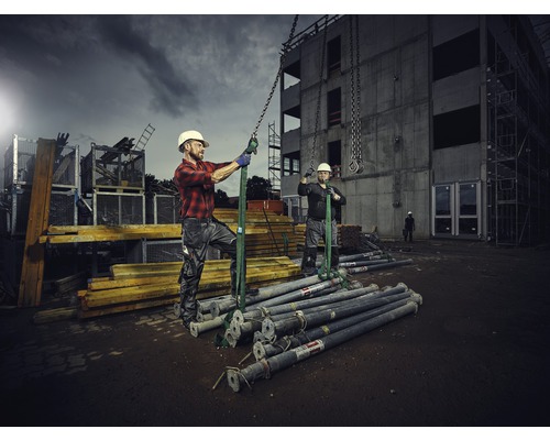 Stavební robotníci zdvíhajú stavebné podpery žeriavom na stavenisku