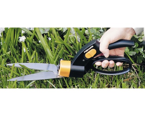 Osoba strihá trávu nožnicami na trávu Fiskars.