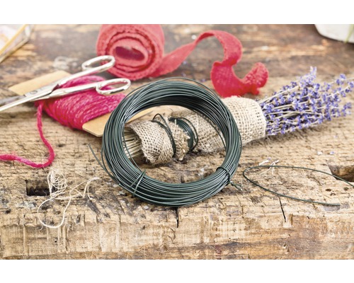 Rolka zeleného floristického drôtu vedľa levandule a darčekovej stuhy na drevenom stole